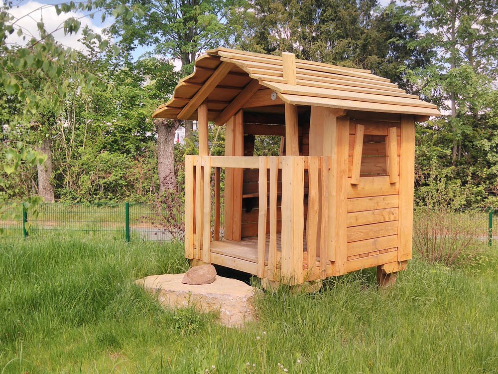 Holzspielhaus für Kindergarten und Spielplatz – individuelle Fertigung Handgefertigtes Spielhaus aus Holz auf naturnahem Außengelände mit Grasfläche