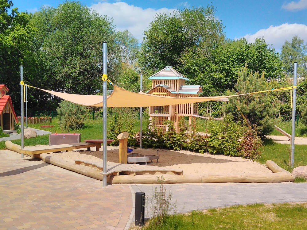 Naturnaher Spielplatz mit Sonnensegel und Holzspielanlage Sandspielbereich mit Sonnensegel, Holzspielhaus und Kletterelementen im Außenbereich